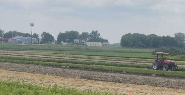 Tractor working in a field with buildings and trees in the background